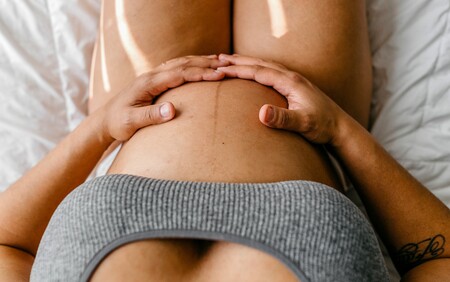 A point of view from a pregnant woman; her hands resting on her tummy.